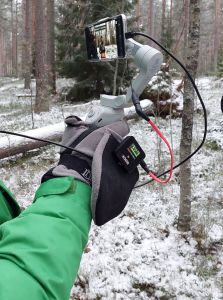 Lähikuva kimbaalissa olevasta matkapuhelimesta, jota henkilö pitää kädessään talvisessa metsässä